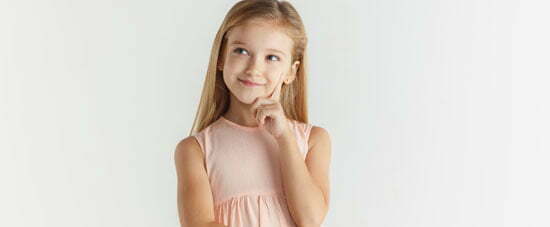 Stylish little smiling girl posing in dress isolated on white studio background. Caucasian blonde female model. Human emotions, facial expression, childhood. Thinking or dreaming,