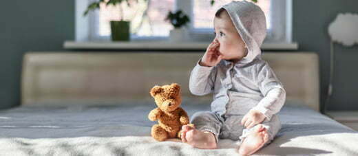 Happy baby boy in grey pyjamas on bed in his room